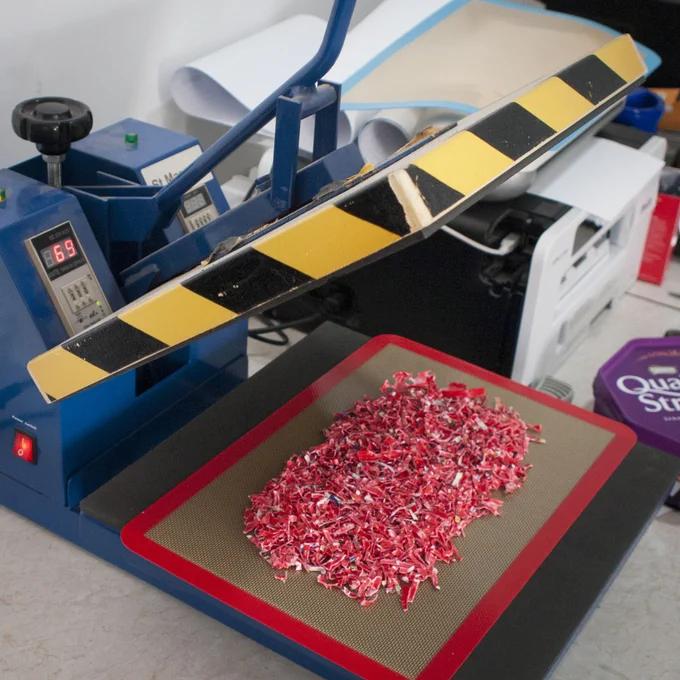 Shredded red sweet tub plastic sitting in a pile inside a heat press, waiting to be melted together into a sheet