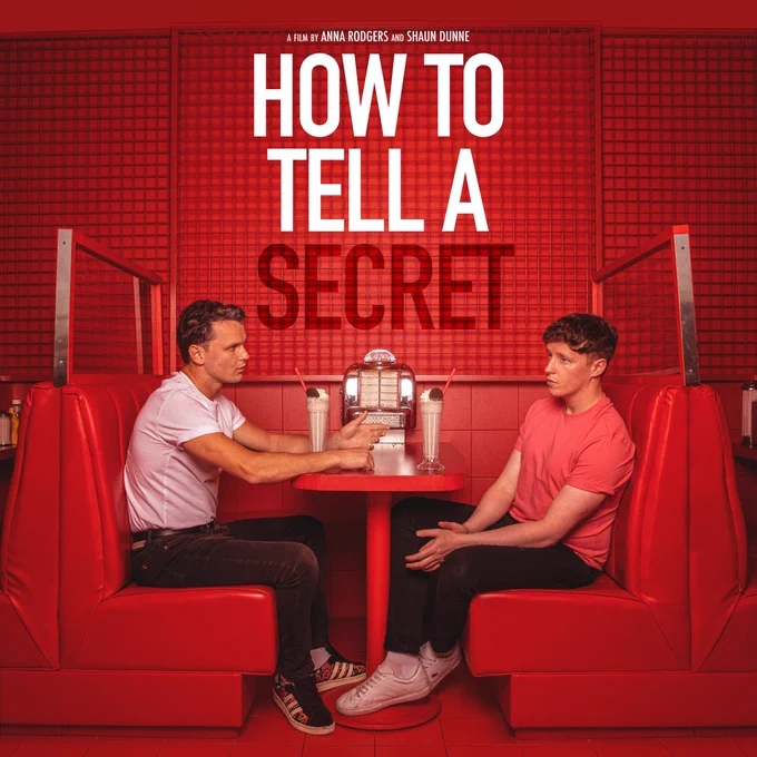 Two men sit in a red booth. Robbie Lawlor and Shane Dunne. Robbie is the central character and Shane is the co-director and writer. Above their booth is the title of the Film: How to Tell a Secret. 
