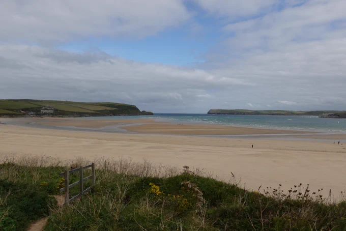 A wide expanse of sandy beach with the seas behind two headlands in the background. The beach is almost completely deserted. 
