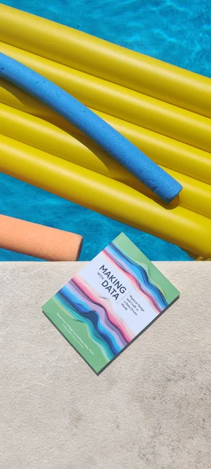 A book near the pool with some colourful pool floats.
