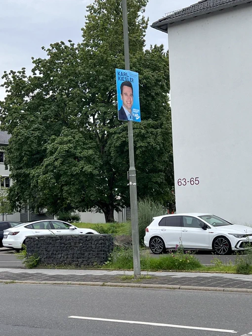 Ein Wahlplakat des AfD Kandidaten Karl Kiesler an einem Laternenmast. Das Plakat ist sehr weit oben angebracht.
