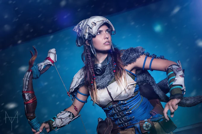 A photo of a cosplay of Aloy from Horizon Zero Dawn, posed drawing an arrow from her quiver and holding her bow.