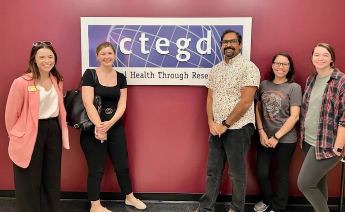  Two congressional staffers are posed next to a professor and two graduate students. Behind them is a sign advertising the Center for Tropical Emerging Global Diseases, located at the University of Georgia
