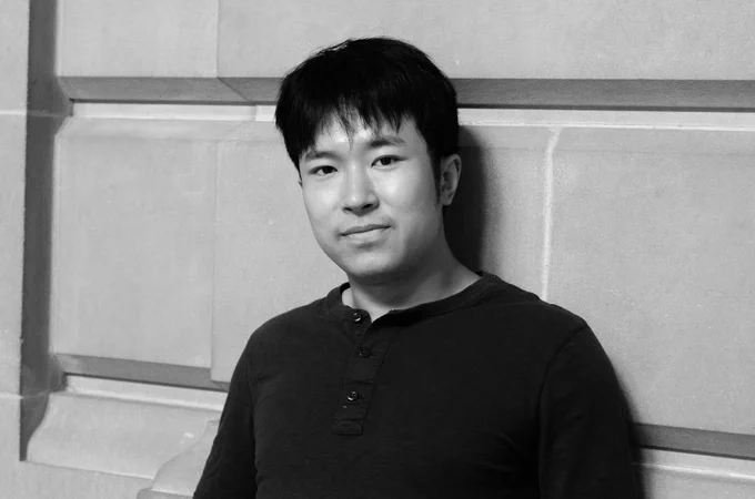 Chen stands against a concrete wall, in black and white