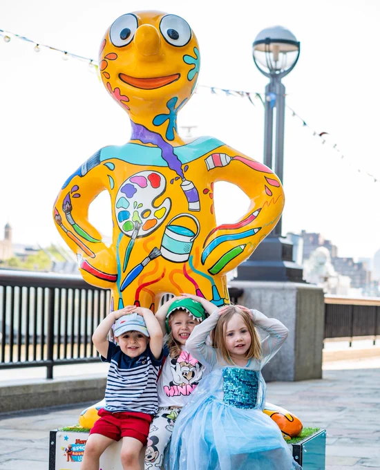 3 children are posing with a Morph statue in London