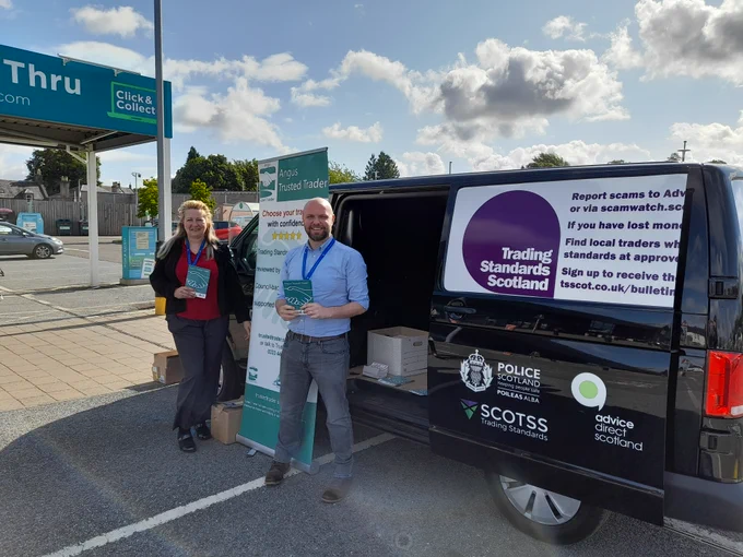 A man and a woman standing in front of a black Trusted Trader awareness scam van