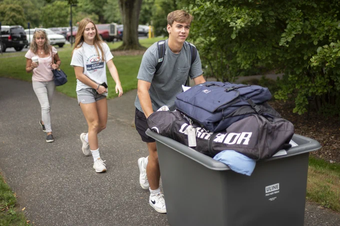 Three people. One is pushing a moving cart.