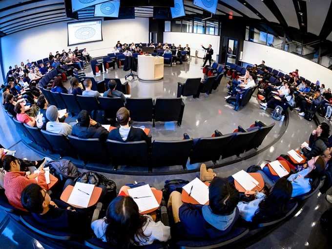 Students work and discuss design projects in a round classroom with numerous monitors hanging from the ceiling and a central podium designed to allow faculty and students to see each other more clearly.