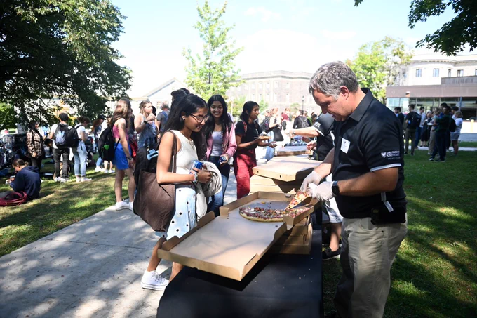 Students are served pizza at an outdoor welcome event