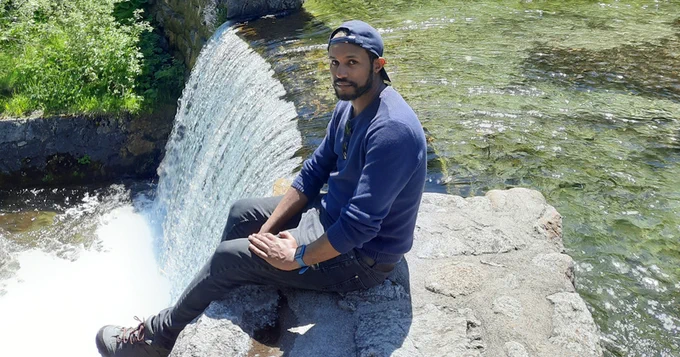 University of Delaware doctoral student Endalkachew Kebede sitting beside a waterfall.