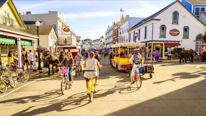 Picture of people biking and horse-drawn wagons and pedestrians in the street on a sunny afternoon on Makinac Island, Michigan, a car-free place in America.