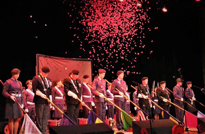 Remembrance Day event

The image shows a stage with two rows of people of different ages in military uniform. The people in the front row are lowering flags. Poppies are falling onto the stage