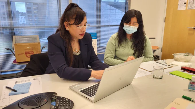 Photo of two women using a laptop. One has a mask