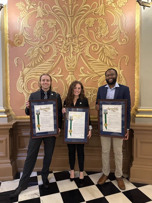 Three Assembly CCST Fellows holding their framed recognitions in the California State Capitol hallway.