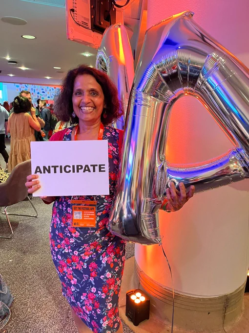 Seetha Kumar with a sign that says 'Anticipate', posing with an inflatable silver A.
