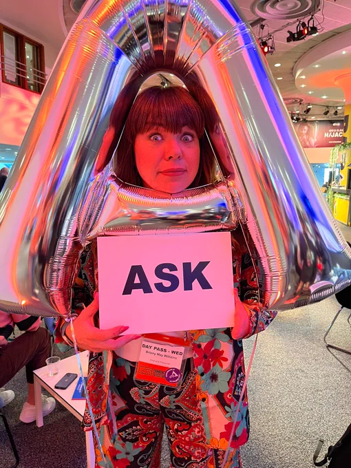 Bryony Mae Williams with a sign that says 'Ask', posing with an inflatable silver A.