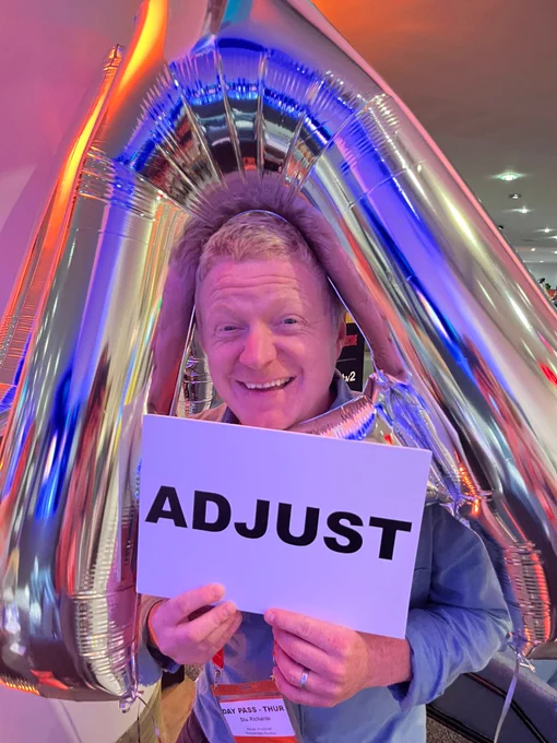 Stu Richards with a sign that says 'Adjust', posing with an inflatable silver A.