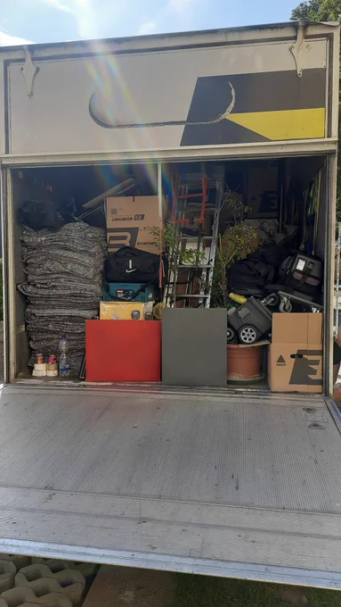 Der Umzugslaster von hinten, er ist sehr voll gepackt mit vielenmöbeln, Kisten Blumen.  Die Sonne scheint