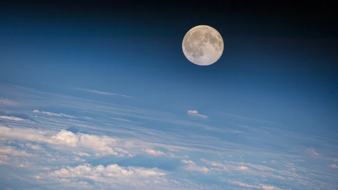 This image of the Moon was taken on Aug. 18, 2016, by NASA astronaut Jeff Williams during Expedition 48 on the International Space Station. The Moon appears full in the top right corner of the image over the white swirling clouds of the Earth below. The sky is a gradient in the background, starting as a soft blue color in the lower portion of the image, and fading softly to black behind the Moon. Credit: NASA
