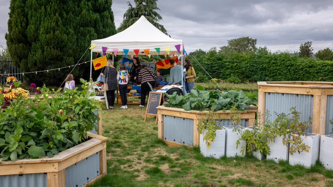 Fairmuir Community Garden. Hexagon raised beds overflow with foliage and people are gathered under a gazebo with colourful bunting hanging from it.