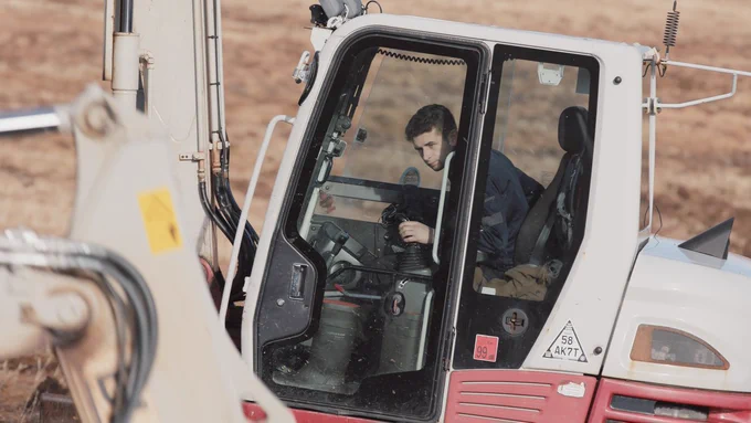 Close-up of a machine operator working in a grey and red excavator cab. 