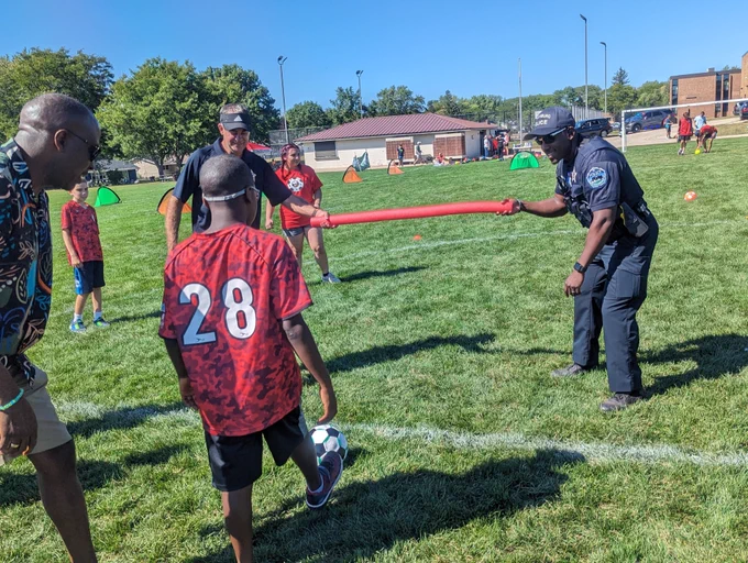 Two Schaumburg Police Officers hold a pool noodle for a TOPSoccer participant to kick a ball under. 