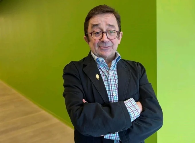 Steven Estey posing and smiling for the camera in front of a green wall. 
