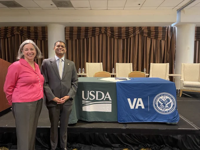Two people smiling standing in front of table. 