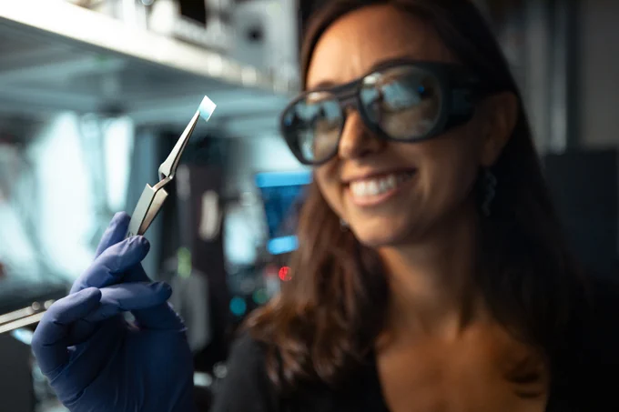 Stanford experimental physicist Halleh Balch holds up a small, square chip the size of a postage stamp.