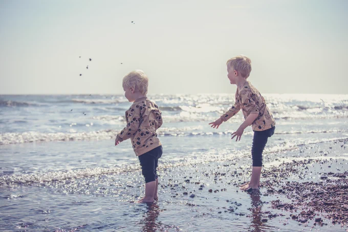 Two children standing by the shore throwing stones into the sea.