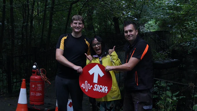 Image one shows three people standing together in the foreground holding the final Soundpath marker before it was installed. In the background there are trees and cones that were used to secure the area when the work was being done.