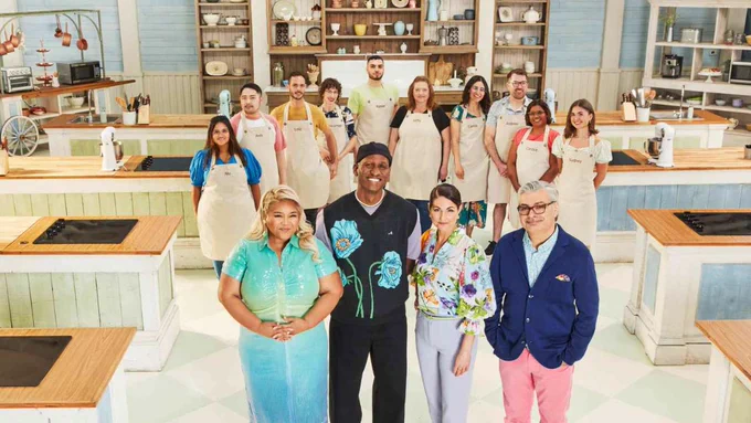 The hosts of the Great Canadian Baking Show stand in the kitchen with ten new contestants behind them in aprons