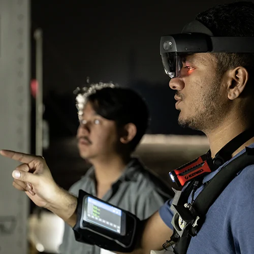 A student wearing a virtual reality visor tests his team's vr interface, while a teammate watches, during the 2023 SUITS competition