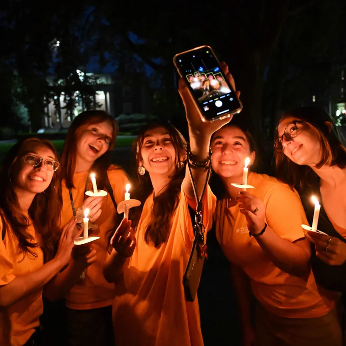 Five students pose for a photo, holding lit candles and smiling at a camera.