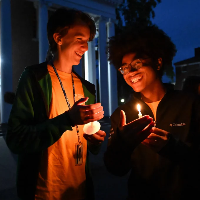 Two students chat and light candles in front of the Chapel.