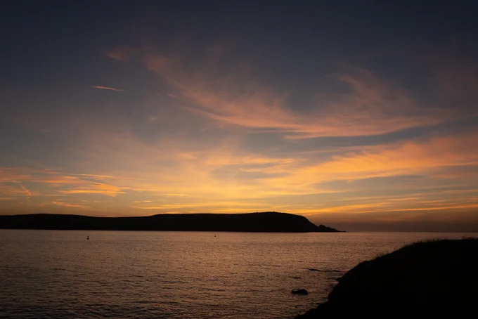 Sunset over an estuary with the water glowing golden in front of dark hills