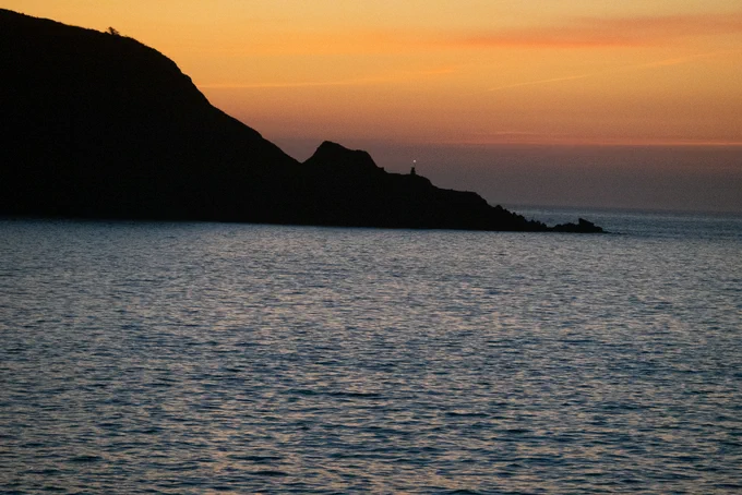 A line of rocks runs down to the sea against a golden sky