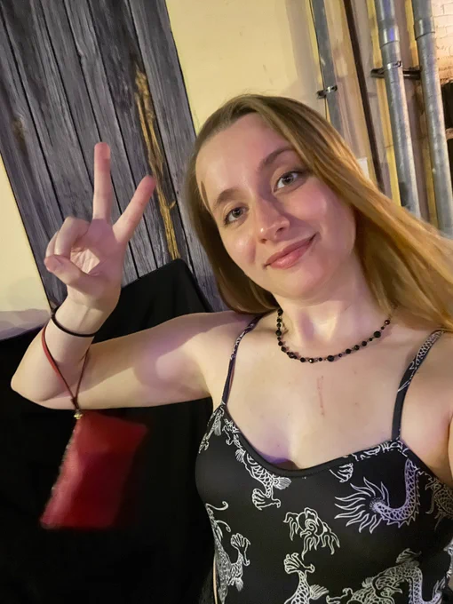 A selfie of Alanis making a peace sign behind a concert venue. She has on a black bodysuit and a black necklace, and she has a cat scratch from Portia on her chest.