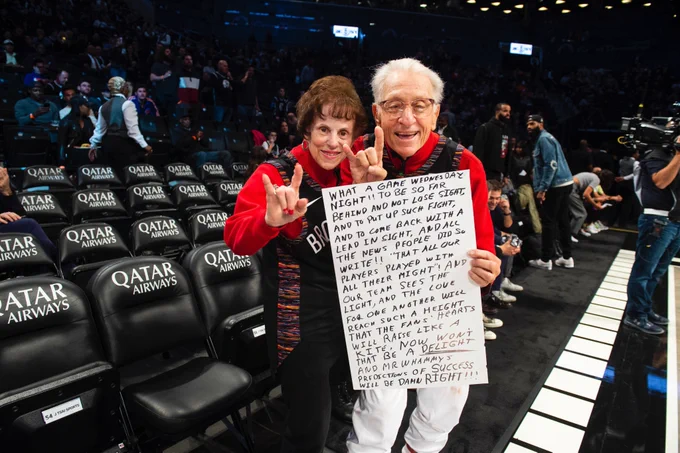 Mr. and Mrs. Whammy courtside pregame with a sign 