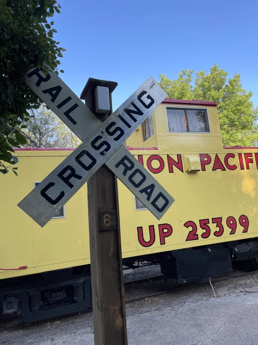 Rail Road crossing sign in front of a yellow caboose.