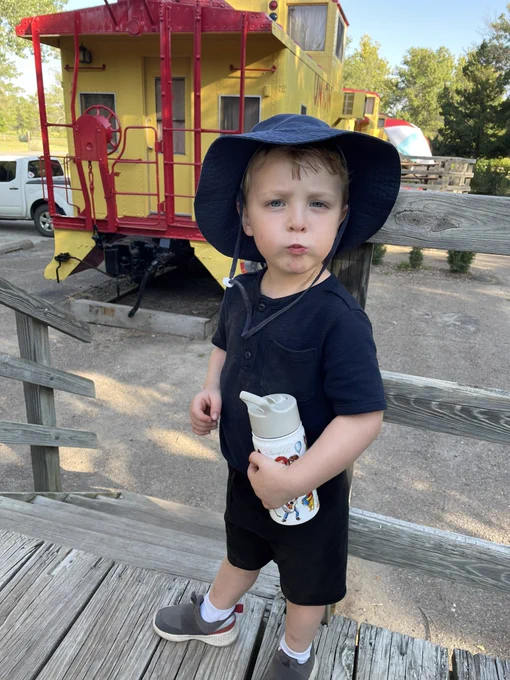 Kennex wearing a hat and holding a water bottle in front of the caboose.