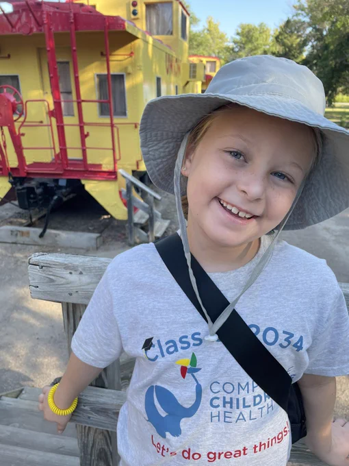 Coralee in a grey hat in front of a yellow caboose.
