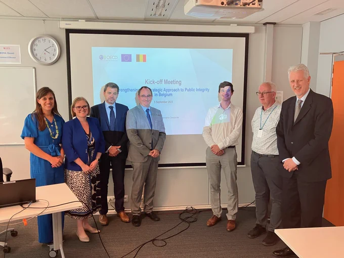 DG REFORM staff standing in front of a projected screensaver with Belgian authorities and OECD staff.