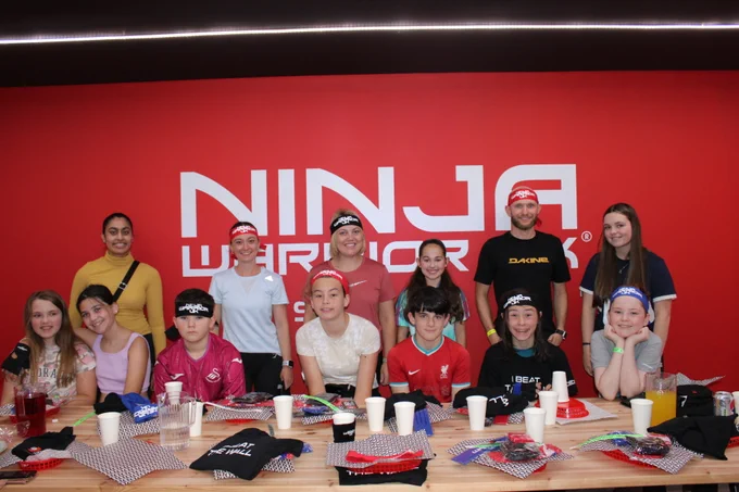 The image shows a group of 13 people having a group photo at Ninja Warrior. 