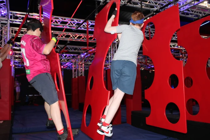 The image shows two young boys climbing on an indoor assault course. 