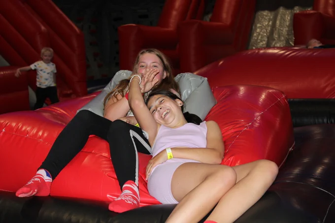 The image shows two young girls on an indoor inflatable assault course having fun. 