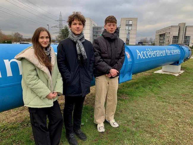 Three students next to a blue pipeline at CERN in France