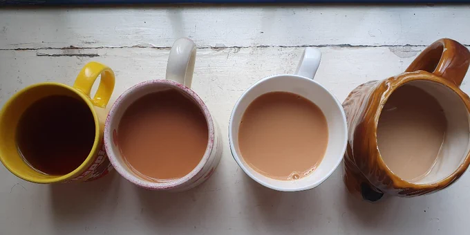 Photograph of four mugs on a window sill. From left to right we have a yellow mug, a white one with faded pink spots, another white mug with yellow lemons and a brown mug in the shape of a star wars character; Chewbacca. Inside each mug is a cup of tea  in varying shades of brown. On the left is a dark brown tea, with no milk. Next along is a dark red tea, then a lighter tea and then a very milky tea on the right at the end. The mugs are supposed to be set up like a colour chart. 