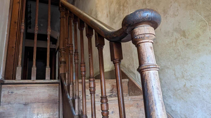 A photograph of a worn wooden bannister attached to a wooden staircase, which leads up to the servants' bedrooms at Dunster Castle.