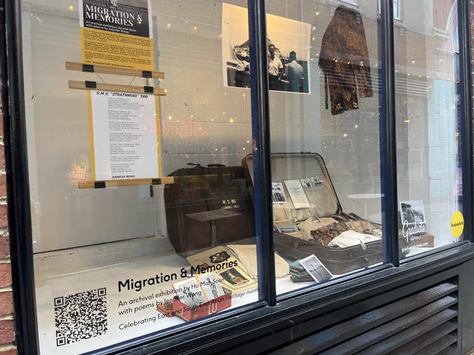Photograph of one of the Migration & Memories gallery windows with a suitcase, clothes, and photographs.
